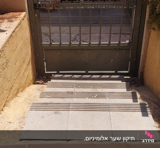 שער מתכת עם שביל מרוצף ופרחים בצדדים